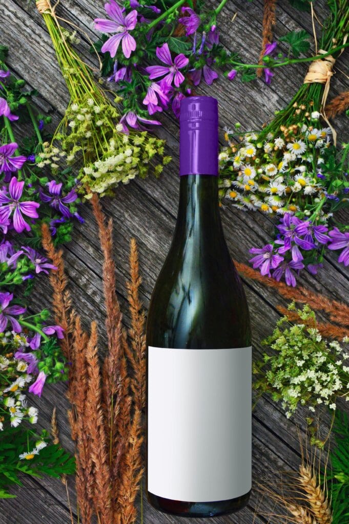 pexels-photo-1479706-1479706-1 A wine bottle surrounded by vibrant purple flowers and greenery on a rustic wooden surface.