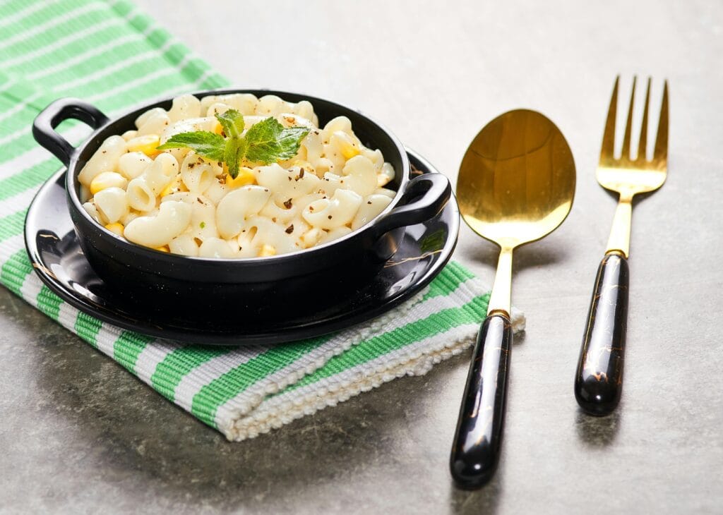 Delicious creamy macaroni in black bowl with fresh herbs, perfect comfort food.