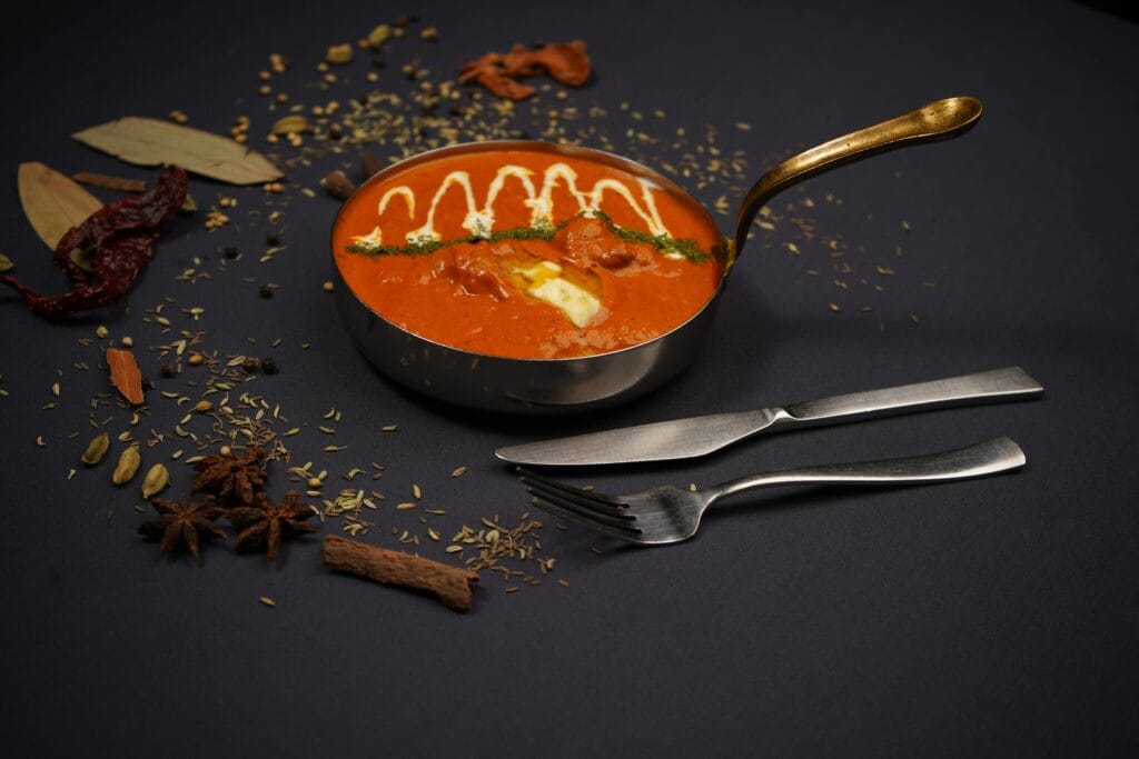 pexels-photo-20408437-20408437 Elegant display of Indian curry with aromatic spices and cutlery on dark background.