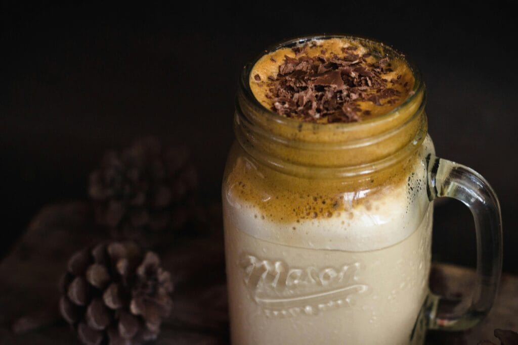 Delicious creamy dalgona coffee topped with chocolate shavings in a mason jar, perfect for a cozy indoor setting.