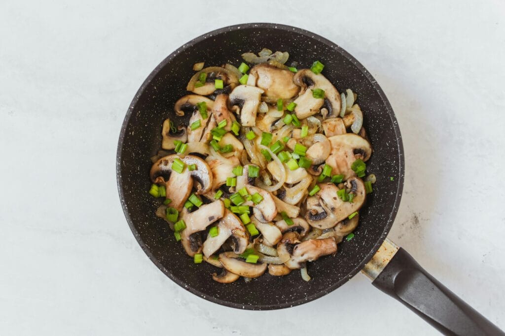 Top view of sautéed mushrooms and spring onions cooking in a frying pan.