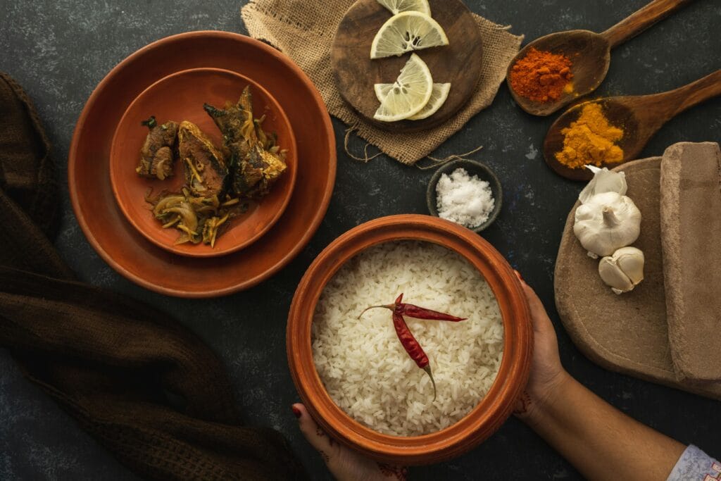 A top view of a traditional Indian meal with rice, spices, garlic, and lemon slices on rustic dishes.