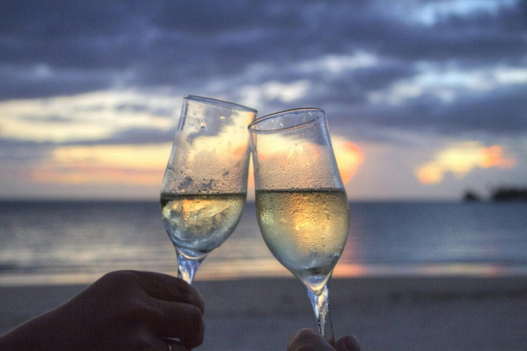 sea-sunset-beach-couple-2145 Two champagne glasses clink at sunset on a serene beach, evoking romance and celebration.